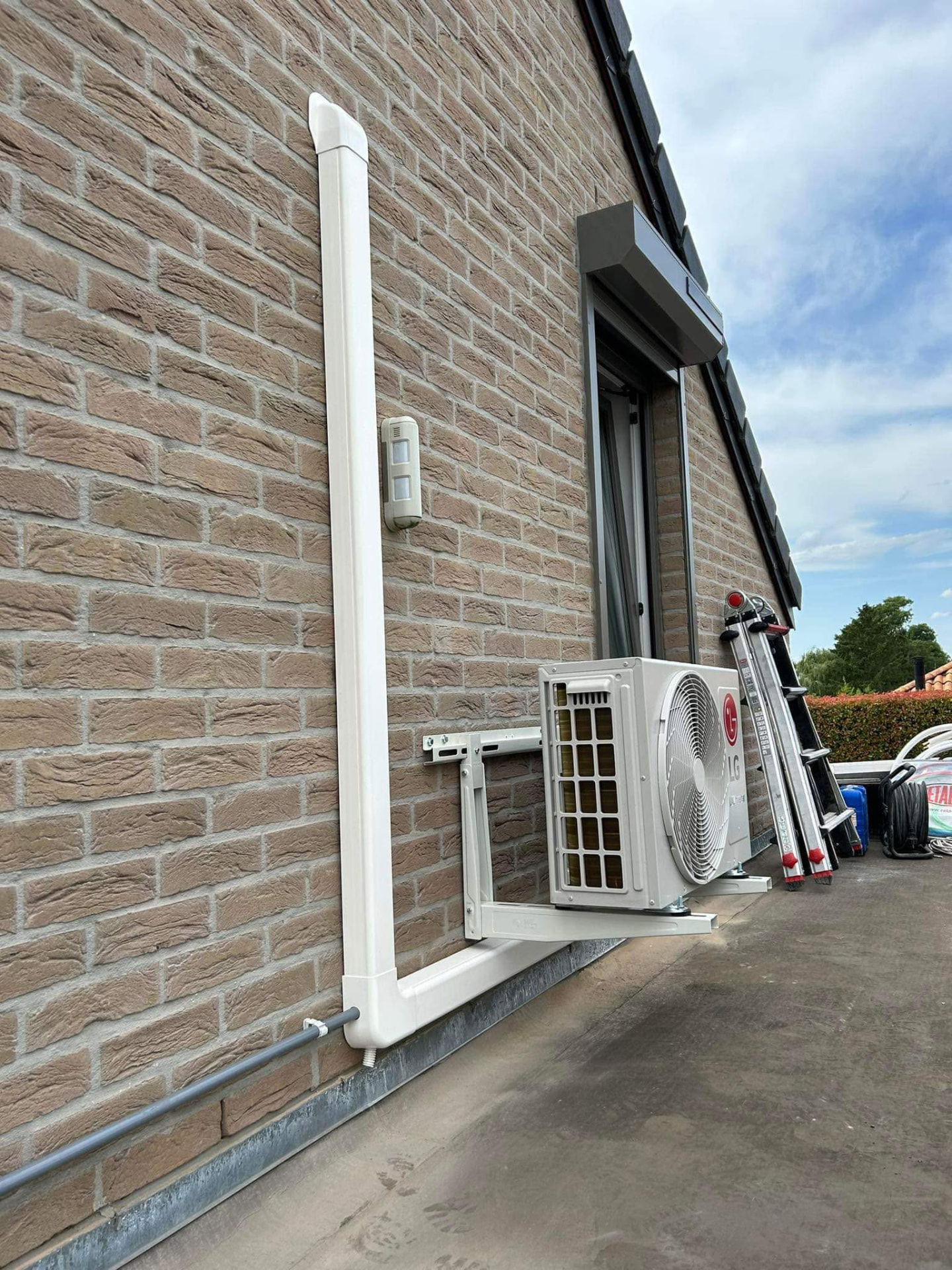 Unité extérieure de climatisation dissimulée en façade par une coiffe de décoration, réalisée par Energies Concept à Binche